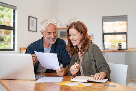 Mature smiling couple sitting and looking at laptop and paperwork for retirement planning.